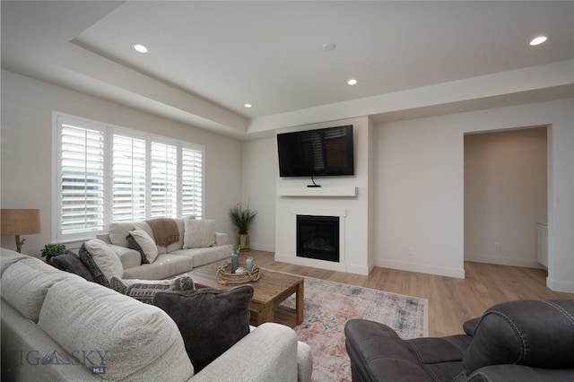 living area featuring light wood-style floors, baseboards, a glass covered fireplace, and recessed lighting