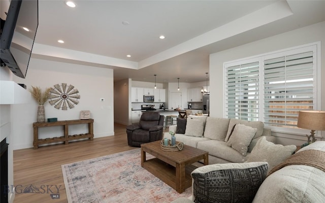 living room with baseboards, a raised ceiling, light wood-style flooring, and recessed lighting