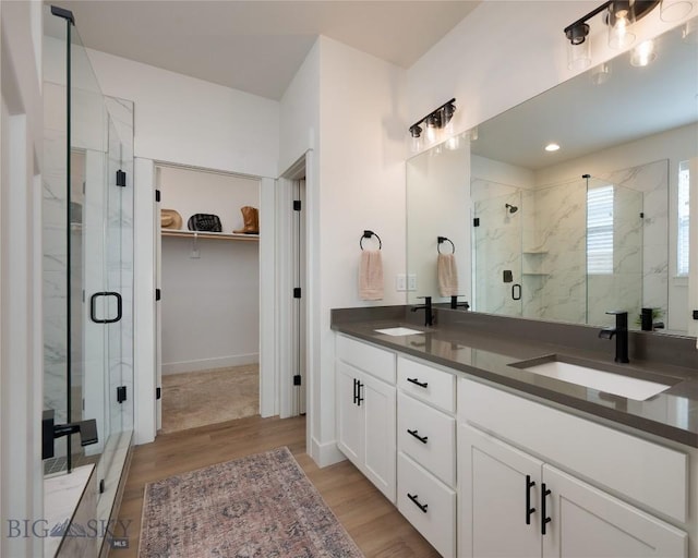 full bath featuring a marble finish shower, wood finished floors, a walk in closet, and a sink