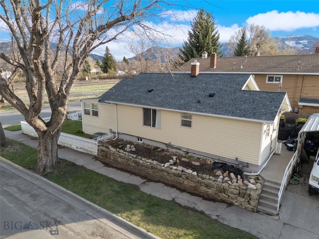 502 W Front St, Livingston, MT 59047 - back of house with a chimney, a shingled roof, a mountain view, and fence