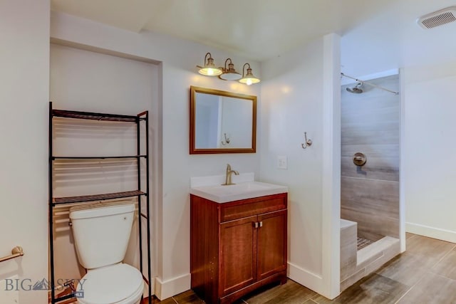 full bathroom with toilet, wood finished floors, vanity, visible vents, and a tile shower