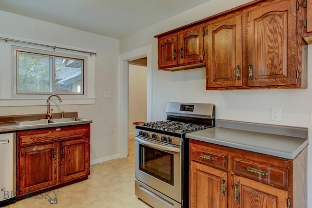 kitchen featuring light floors, dishwasher, baseboards, a sink, and stainless steel range with gas stovetop