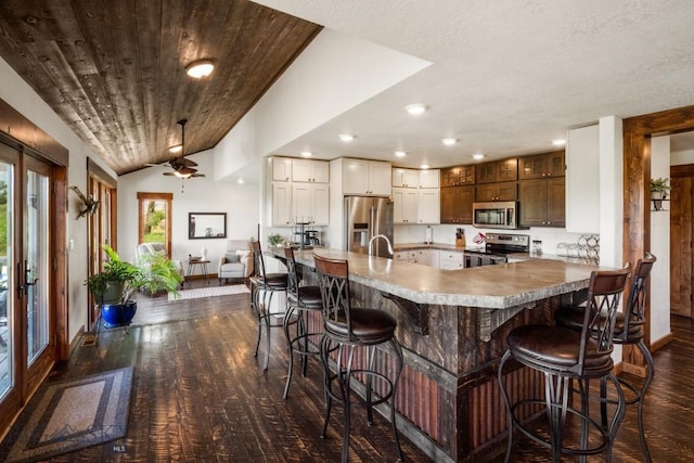 kitchen featuring a peninsula, appliances with stainless steel finishes, dark wood-style floors, and a kitchen bar