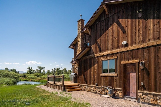 view of side of property featuring a yard, a chimney, and a deck with water view