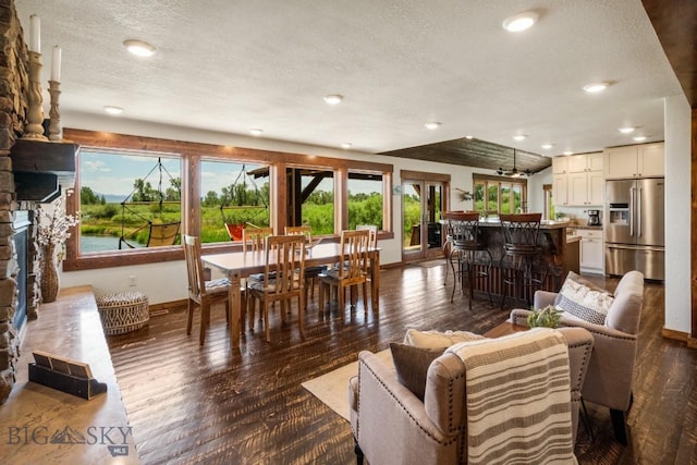 living area featuring recessed lighting, a textured ceiling, baseboards, a stone fireplace, and dark wood-style flooring
