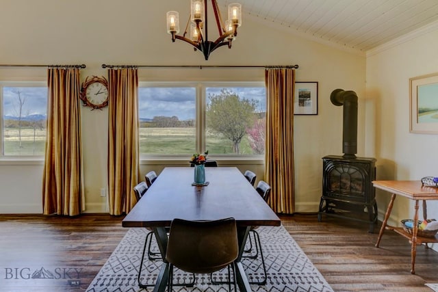 dining space with wood finished floors, a wood stove, ornamental molding, vaulted ceiling, and a chandelier