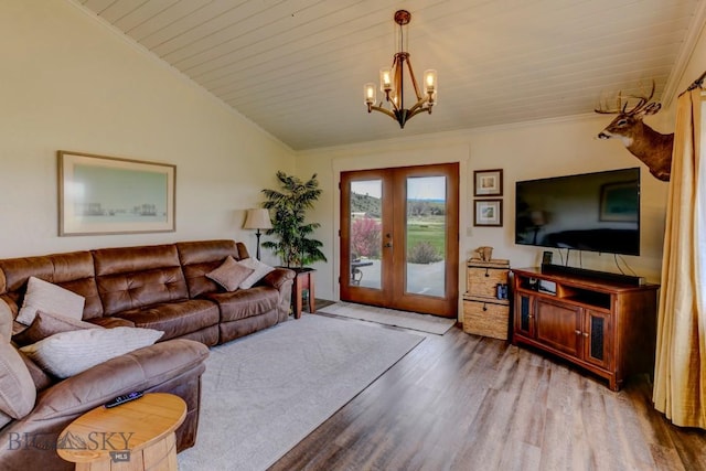 living room featuring lofted ceiling, a notable chandelier, french doors, ornamental molding, and wood finished floors