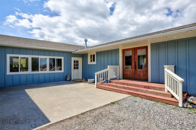 doorway to property with board and batten siding, roof with shingles, a patio, and french doors