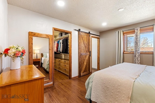 bedroom featuring wood finished floors, a textured ceiling, a barn door, baseboards, and recessed lighting