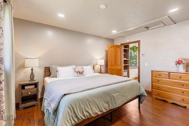 bedroom with attic access, a textured ceiling, wood finished floors, and recessed lighting