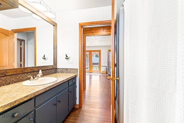 full bathroom with a shower with shower curtain, wood finished floors, vanity, and backsplash