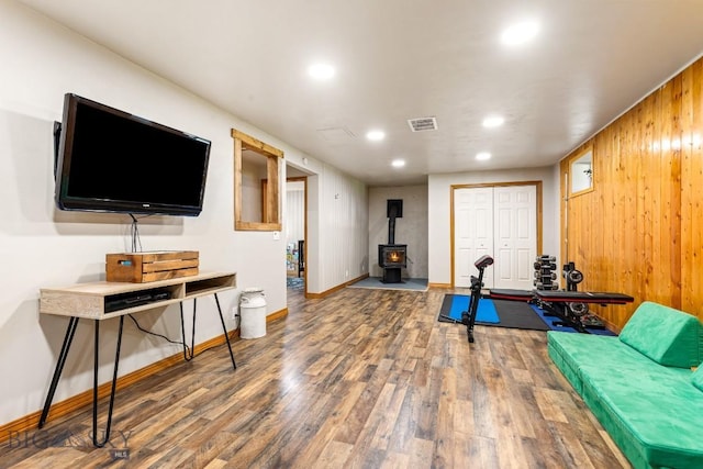 exercise room featuring wood walls, wood finished floors, a wood stove, recessed lighting, and baseboards