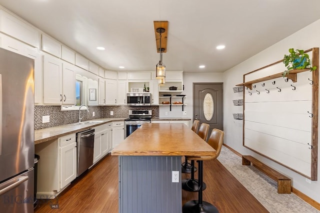 kitchen with a breakfast bar, open shelves, a sink, white cabinetry, and appliances with stainless steel finishes
