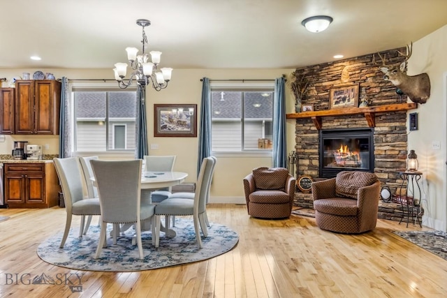 dining area featuring light wood finished floors, a chandelier, a stone fireplace, and baseboards