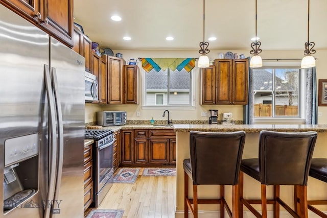 304 Farmall Ln, Manhattan, MT 59741 - kitchen featuring appliances with stainless steel finishes, light wood-style flooring, a sink, a breakfast bar, and light stone counters