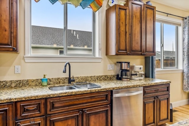kitchen with dishwasher, a sink, light stone countertops, and light wood finished floors