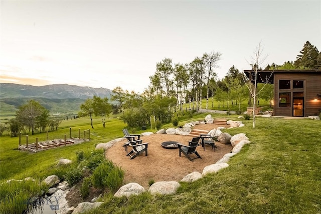 view of green lawn with an outdoor fire pit and a mountain view