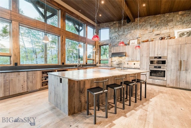 kitchen with wood ceiling, a towering ceiling, light wood finished floors, under cabinet range hood, and a spacious island