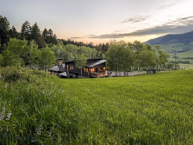 back of property featuring a lawn, a deck with mountain view, a chimney, and metal roof