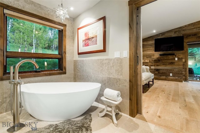 bathroom with a freestanding tub, tile walls, and lofted ceiling