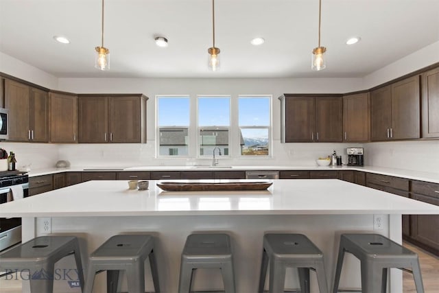 kitchen featuring a sink, a kitchen bar, dark brown cabinets, appliances with stainless steel finishes, and light countertops