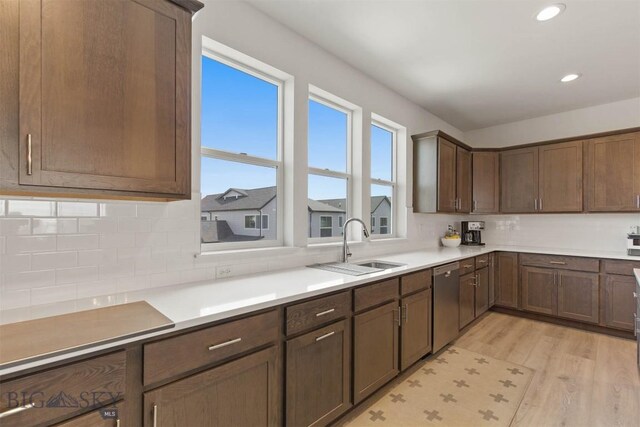 kitchen featuring stainless steel dishwasher, a sink, light wood-type flooring, recessed lighting, and backsplash