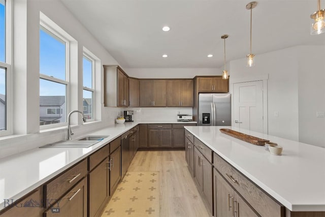 kitchen with stainless steel appliances, a sink, light wood-style floors, recessed lighting, and decorative light fixtures