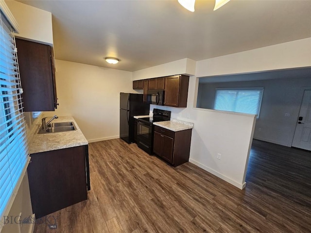 kitchen featuring black appliances, a sink, dark brown cabinetry, baseboards, and dark wood finished floors