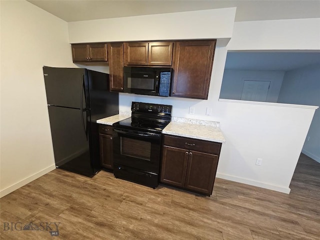 kitchen featuring black appliances, dark brown cabinetry, light countertops, and light wood-style flooring