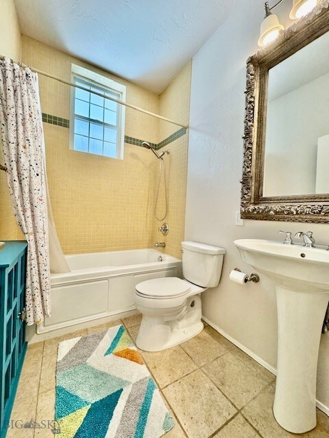 full bath with shower / bathtub combination with curtain, toilet, tile patterned floors, baseboards, and a sink