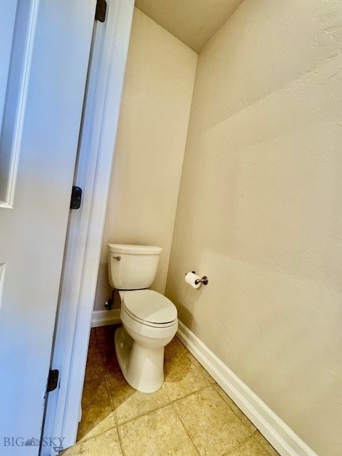 bathroom with toilet, baseboards, and tile patterned flooring