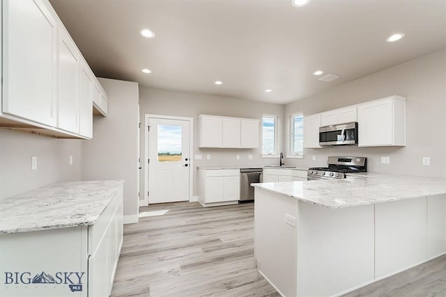 kitchen with appliances with stainless steel finishes, a peninsula, a sink, white cabinetry, and recessed lighting