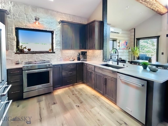 kitchen featuring stainless steel appliances, a sink, a peninsula, light countertops, and light wood-type flooring