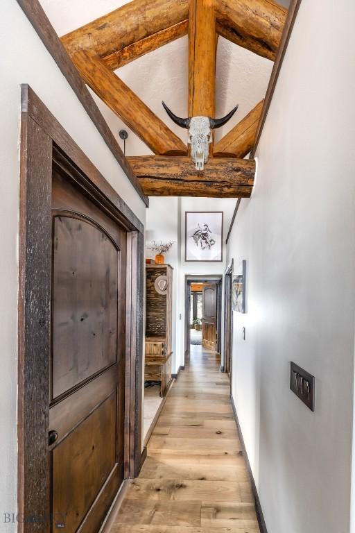 corridor featuring light wood-style floors, beamed ceiling, and baseboards