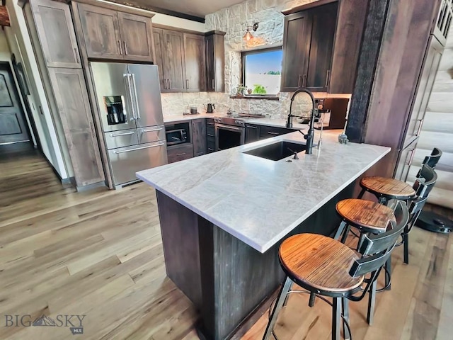 kitchen with stainless steel appliances, a sink, a peninsula, light wood-style floors, and backsplash