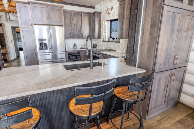 kitchen with appliances with stainless steel finishes, light wood-style floors, decorative backsplash, a sink, and a breakfast bar
