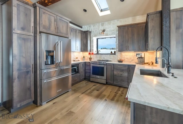 kitchen featuring stainless steel appliances, a sink, a skylight, light stone counters, and decorative backsplash