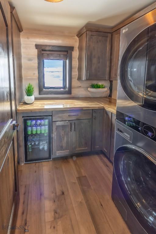 laundry area with wine cooler, stacked washer and clothes dryer, cabinet space, and dark wood-style flooring