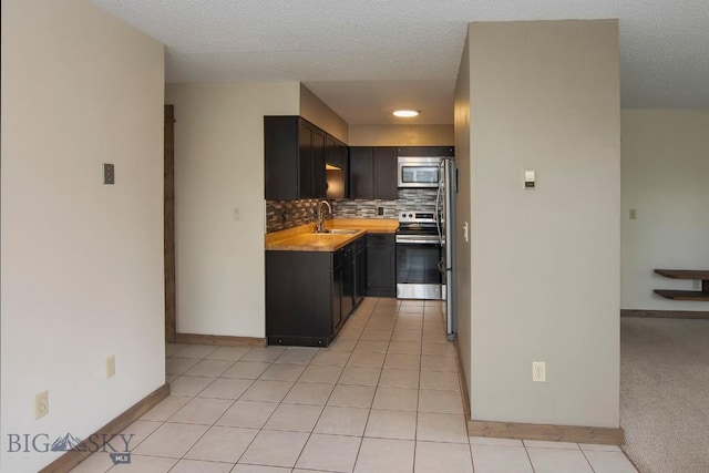 kitchen featuring stainless steel appliances, a sink, light countertops, backsplash, and light tile patterned floors