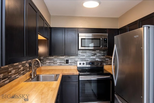 kitchen with appliances with stainless steel finishes, a sink, decorative backsplash, and wood counters