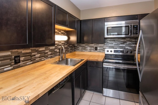 kitchen with stainless steel appliances, wood counters, a sink, and light tile patterned floors