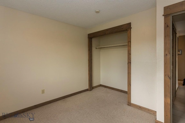 unfurnished bedroom featuring light colored carpet, baseboards, a closet, and a textured ceiling