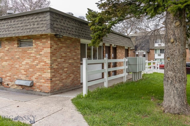 view of property exterior featuring mansard roof, brick siding, fence, and roof with shingles