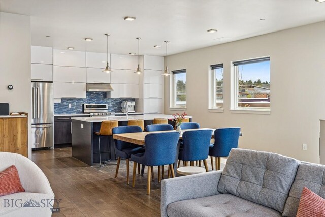 kitchen with appliances with stainless steel finishes, modern cabinets, under cabinet range hood, a kitchen bar, and white cabinets