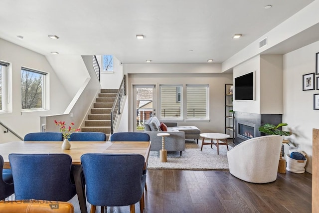 living area with stairs, dark wood-type flooring, healthy amount of natural light, a glass covered fireplace, and recessed lighting