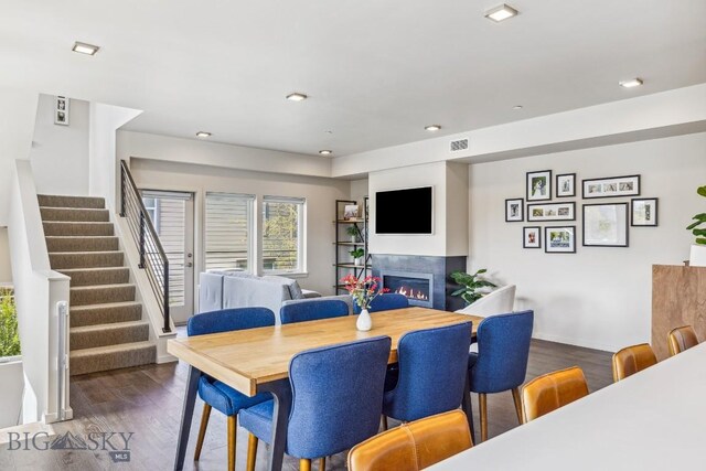dining room with wood finished floors, a warm lit fireplace, stairs, recessed lighting, and baseboards