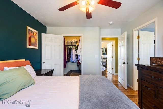 bedroom with wood finished floors, a ceiling fan, a spacious closet, a closet, and baseboards