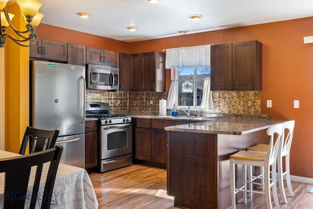kitchen featuring stainless steel appliances, light wood-style floors, a peninsula, decorative backsplash, and a breakfast bar