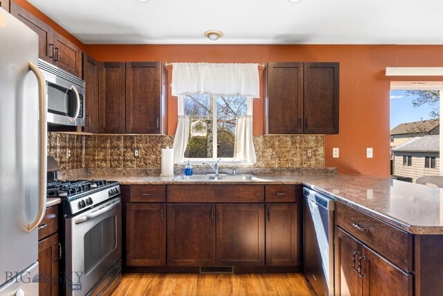 kitchen with stainless steel appliances, a sink, a peninsula, and tasteful backsplash