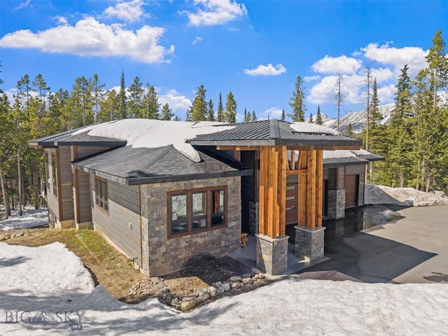 modern home featuring roof mounted solar panels, stone siding, and driveway